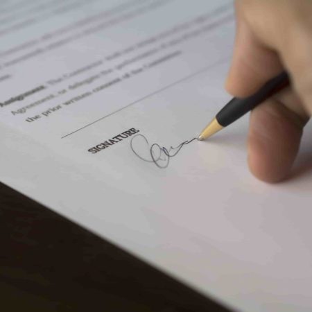 Person Signing a Document with a Black Pen